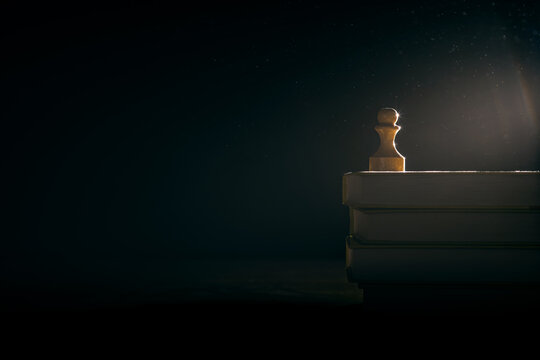 A white wooden pawn stands on a stack of old vintage books. Mock up. Blank space for text