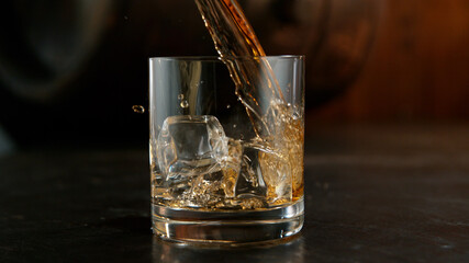 Glass of whisky with splashing liquid and ice rocks inside.