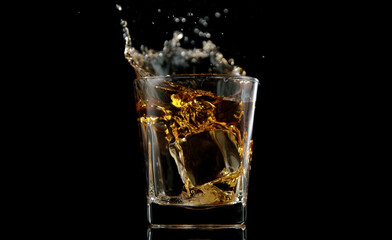 Glass of whisky with splashing liquid and ice rocks inside.