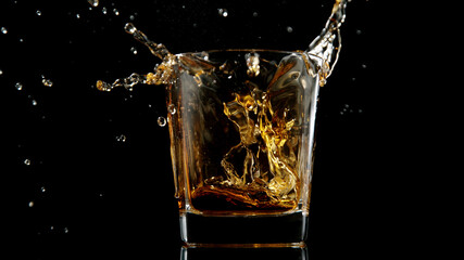 Glass of whisky with splashing liquid and ice rocks inside.
