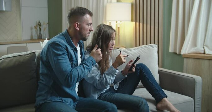 Happy young couple are enjoying their victory at home on the couch. We saw our victory on the mobile phone. High quality 4k footage