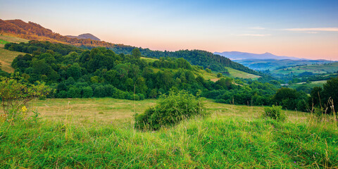 Fototapeta na wymiar mountainous rural landscape at dawn. beautiful scenery with forests, hills and meadows in morning light. ridge with high peak in the distance. village in the distant valley