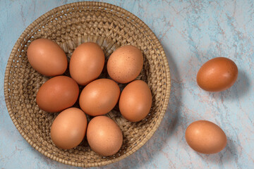 several fresh chicken eggs in a straw basket on a wooden background. Healthy eating concept.