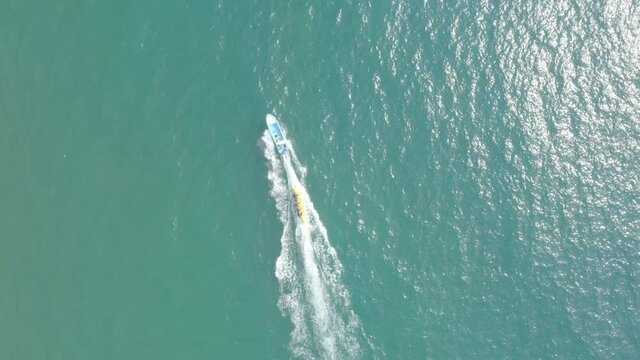 Aerial top view of a banana boat ride, slowly zooming in at het banana boat that tips over