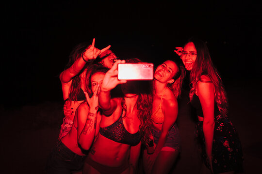 Group of young women having fun at a lakeside party at night with a red light