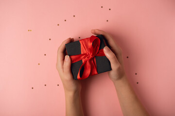Woman's hand holding black gift box with red ribbon on the rose background. The Concept Of Valentine's Day.