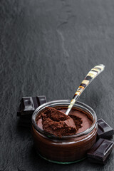 Dark chocolate mousse with ganache in glass jar on black stone background