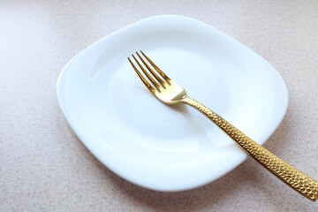 White plate with a golden fork on a gray table, side view, close-up