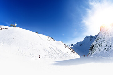 Fototapeta na wymiar winter snow landscape in high mountain range against blue sky with clouds background. Panorama wide view of mountains with people walking down to valley. New year white christmas wallpaper