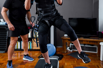 Fototapeta na wymiar Woman training at home with an electrostimulation vest and dumbbells with the supervision of a personal trainer
