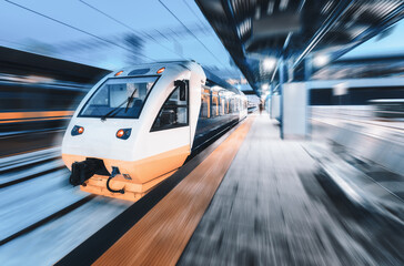 Fototapeta premium High speed train in motion on the railway station at night. Modern intercity passenger train with motion blur effect on the railway platform. Industrial. Railroad in Europe. Commercial transportation