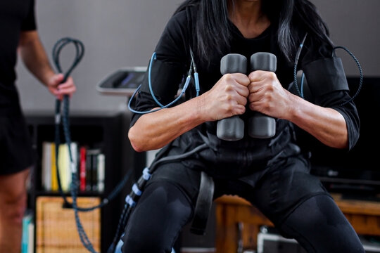 Woman training at home with an electrostimulation vest and dumbbells with the supervision of a personal trainer