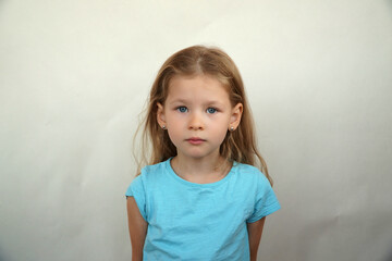 Fototapeta premium Cute little girl shows emotions on a white background in a T-shirt. Simple beauty. High quality photo