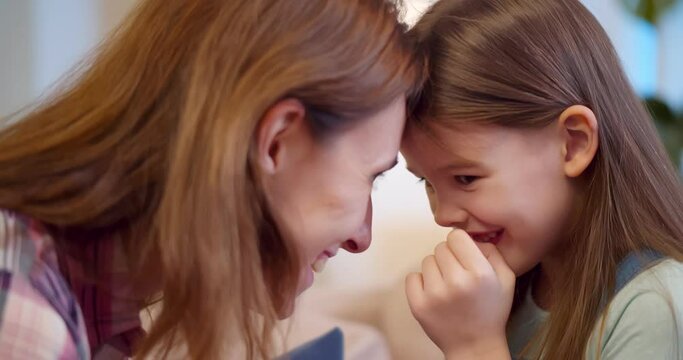 Joyful mom sitting with little girl on couch hugging and cuddling
