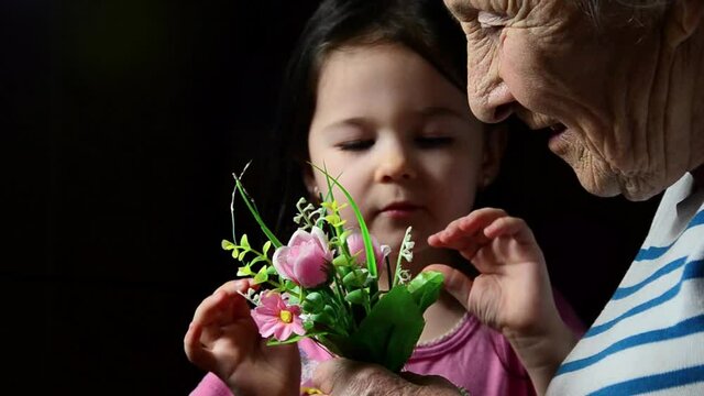 The child gives flowers to an old grandmother. Flowers in mother's wrinkled hands. Baby and old hands with flowers. Goodness concept. Grandmother and child with flowers. Happy family on a holiday
