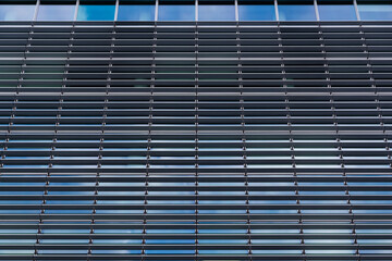Elevation of modern office building with external horizontal blinds and reflection of the blue sky...