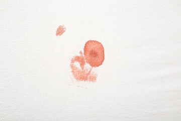 Red fresh blood stain on white sheet after night menstruation. Closeup. Top down view.