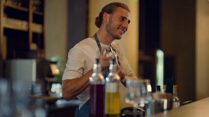 Sexy barman mixing cocktails at counter. Bartender talking unknown visitors.