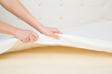 Young adult woman hands opening white cover and showing yellow rubber foam inside orthopedic mattress. Closeup.