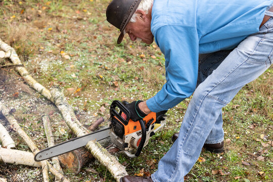 Senior man working with a chainsaw during cutting trunks for firewood in his backyard. - Powered by Adobe