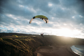 Gente haciendo parapente en un acantilado con la playa debajo y un atardecer 