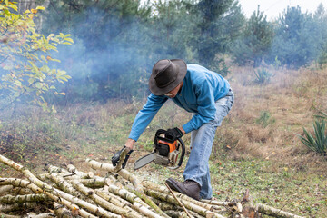 Handsome senior man working with a chainsaw during cutting trunks for firewood in his backyard.