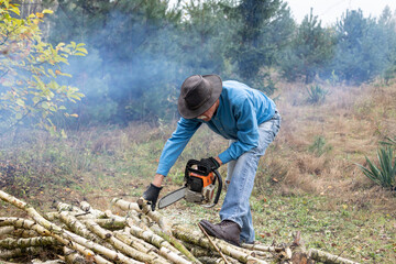Handsome senior man working with a chainsaw during cutting trunks for firewood in his backyard.