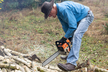 Handsome senior man working with a chainsaw during cutting trunks for firewood in his backyard.