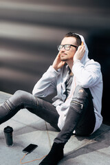 Smiling man listening music over headphones while relaxing on a sidewalk.