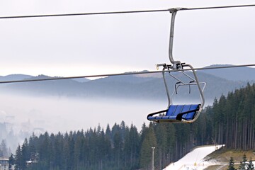 empty ski lift seats going down on blurred background of mountain landscape in fog