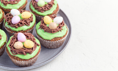 Homemade carrot cupcakes with cream cheese frosting and Easter chocolate eggs, on  gray plate, horizontal, copy space, closeup