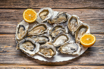 Fresh opened oysters in a white plate with lemon on dark wooden textured background, top view