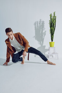 The Guy Is Kneeling In A Bright Room Near A Flower And Fashionable Clothes Style