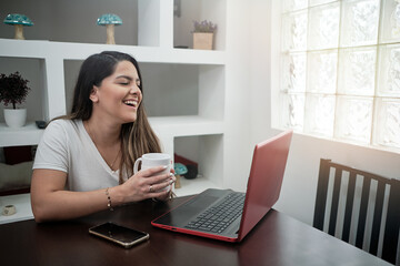 Latin girl smiling sitting watching the computer and the cell phone