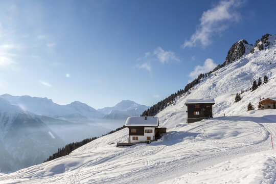 Swiss chalets on the Alps with ski slopes in winter sprorts resort with morning fog and mist rising up the valley