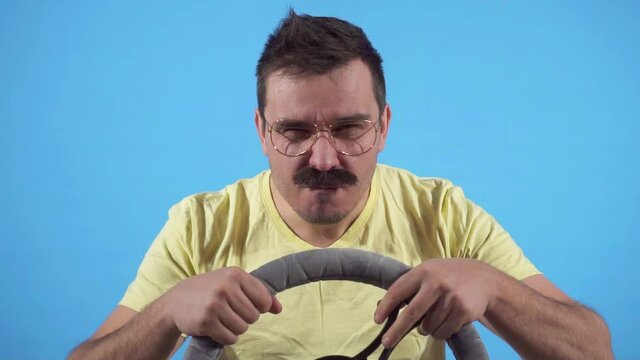 Focused man with a mustache behind the wheel on a blue background slow mo, isolate