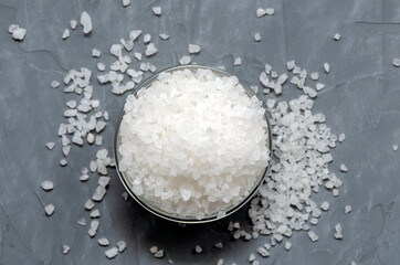 coarse white sea salt in a glass bowl is scattered on the table - top view. On a gray concrete background.