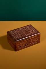Old vintage handcarved wooden box in a dark brown color on a yellow surface with a green background. An antique authentic handmade woodcarved treasure container. Vertical Shot