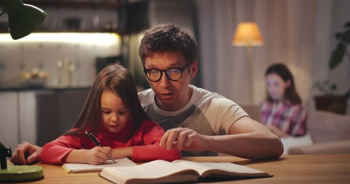 Father helping daughter with homework sitting at table together