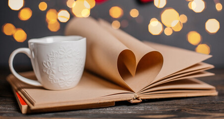 Heart made from book sheets with a cup in lights, love and valentine concept on a wooden table
