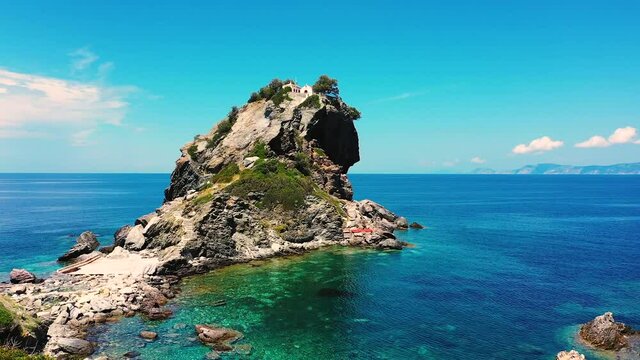 Drone taking off near a small chapel and church on the top of a small cliff close to Agios Ioannis Skopelos beach in Greece. The sea in the background is beautiful and clear blue. 1080p