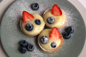 French portion dessert. Little tarts with custard, fresh berries and powdered sugar. Tartlets with strawberries, blueberries served with icing sugar (castor sugar) on gray and white plates
