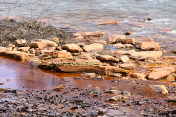 Orange acid abandoned coal mine drainage water entering clean water stream with rocks in Western Pennsylvania
