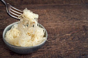 Fermented cabbage on a fork above a bowl, with copy space