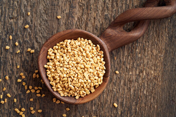 Fenugreek seeds on a wooden spoon on a table, top view