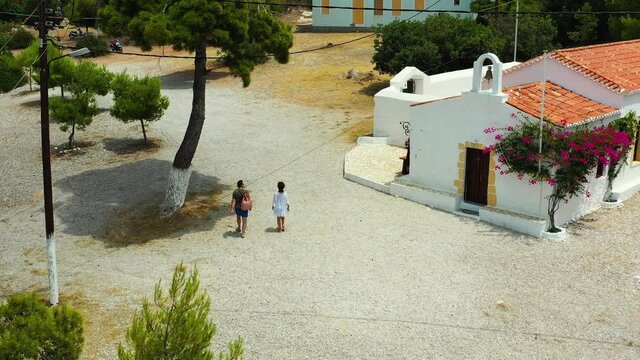 Drone flying backwards over Agia Paraskevi Spetses beach in Greece. The drone starts over land, and fly out over sea. There are a couple leaving the beach, and there are few people lying on the beach