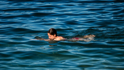 A young girl swims in the crystal clear water of a mountain lake.