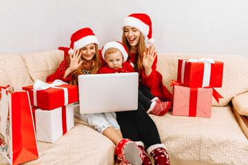mother and two small children in Santa Claus hats, are having a Christmas party, video conference...