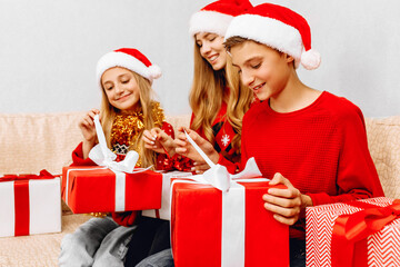 Happy family, a young mother and her little daughter and son, wearing santa claus hats