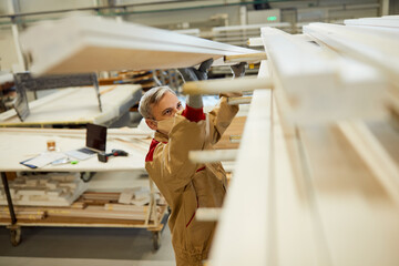 Carpenter with face mask while taking wood planks from a shelf in a workshop.